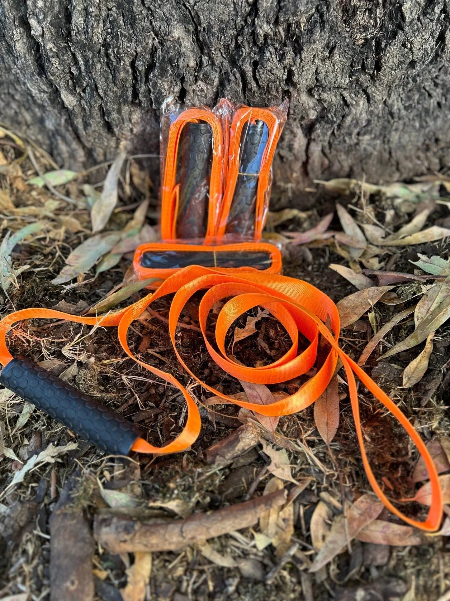 Orange deer recovery drag rope with black handles on forest ground near tree trunk